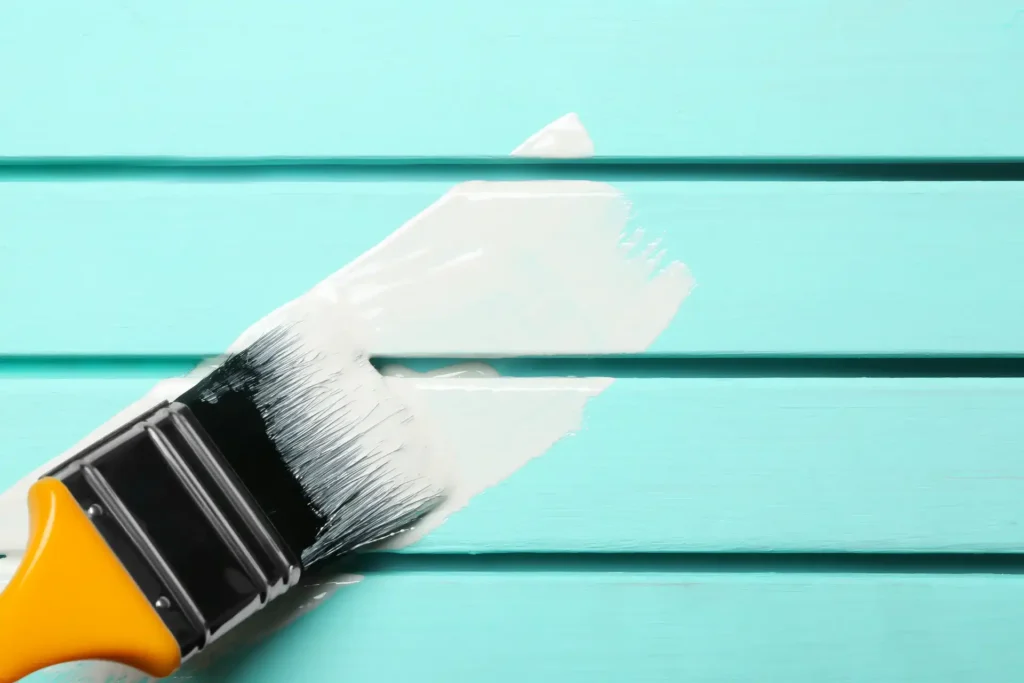 Brush applying white paint on deck boards for What Is the Best Deck Paint guide