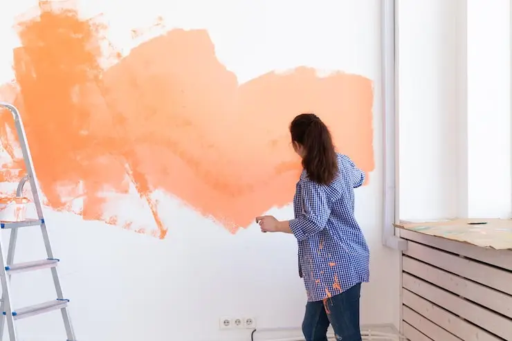 Woman painting a room with orange paint — illustrating how long it takes to paint a room.