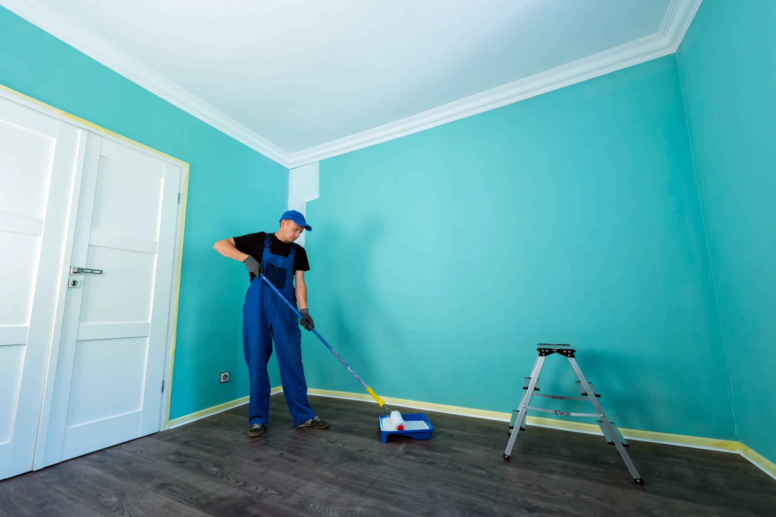 Professional house painter applying white paint on turquoise wall using roller – Intercolor Painting LLC interior painting service in Seattle